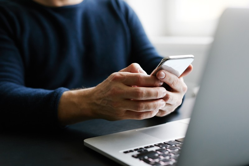 Man with Blue Jumper Holding Phone at Laptop